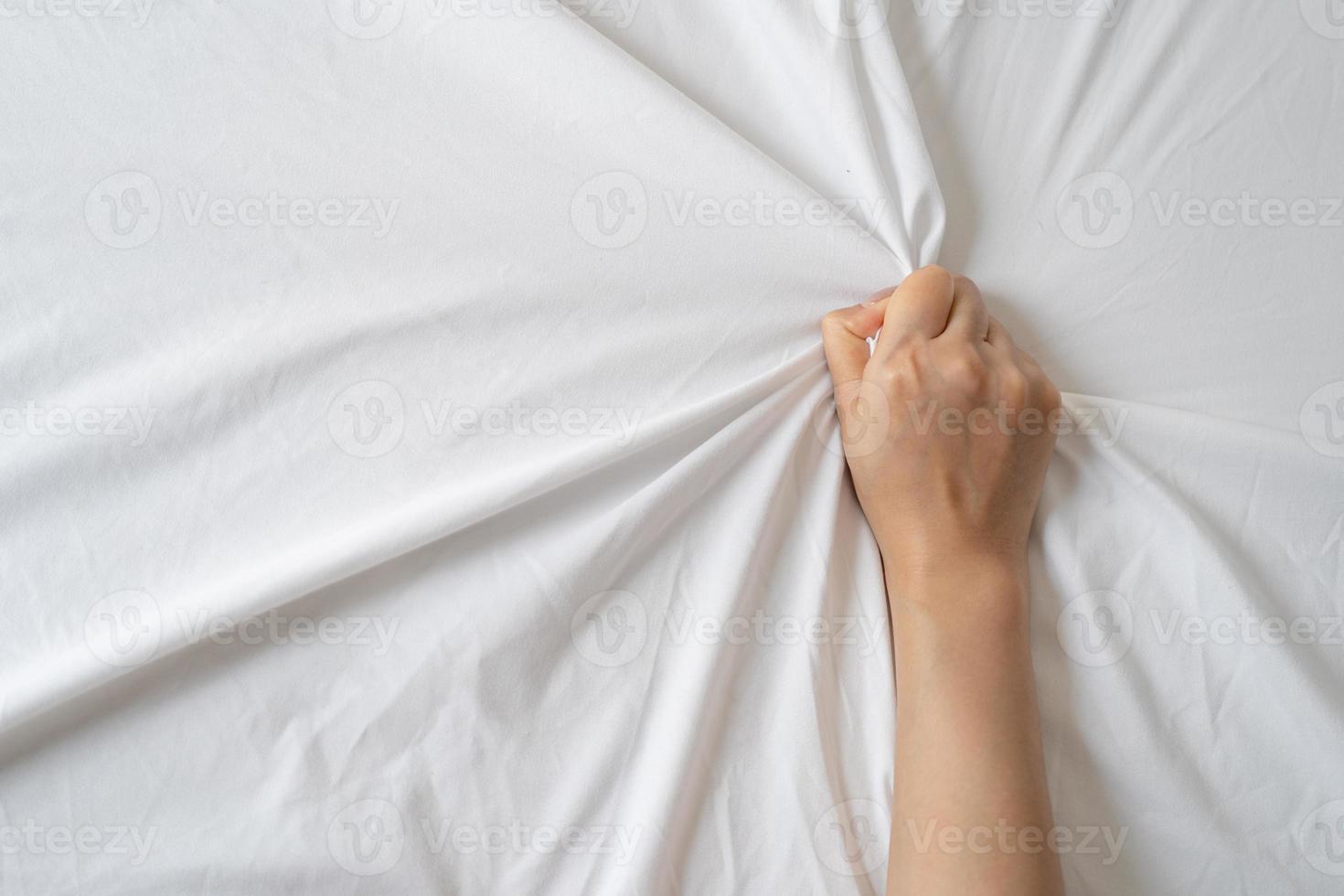 Top view of young sexy woman hands pulling white sheets in orgasm. Sex concept. photo