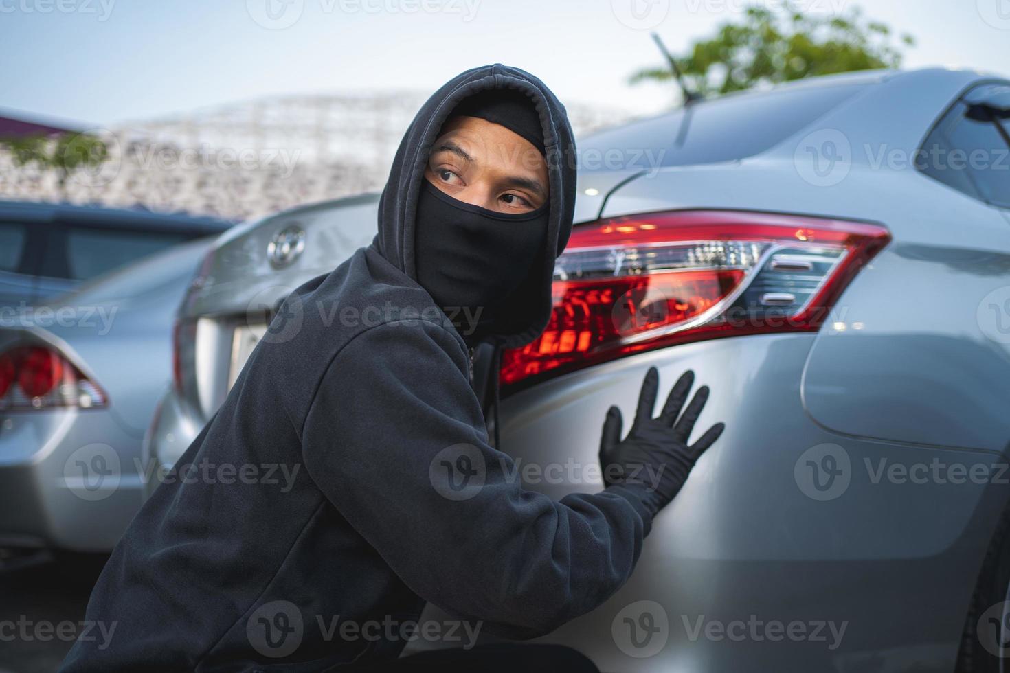 Terrorist or car thief in black mask with car. robbery and crime concept. photo