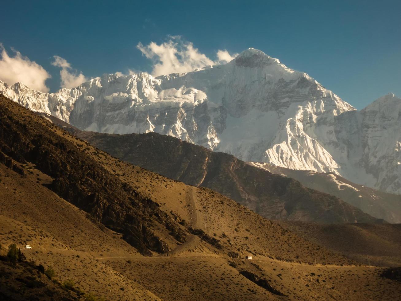 The Nilgiri North mountain towering over the sandy hills surrounding the village of Kagbeni on the Annapurna Circuit trekking trail in Nepal. photo