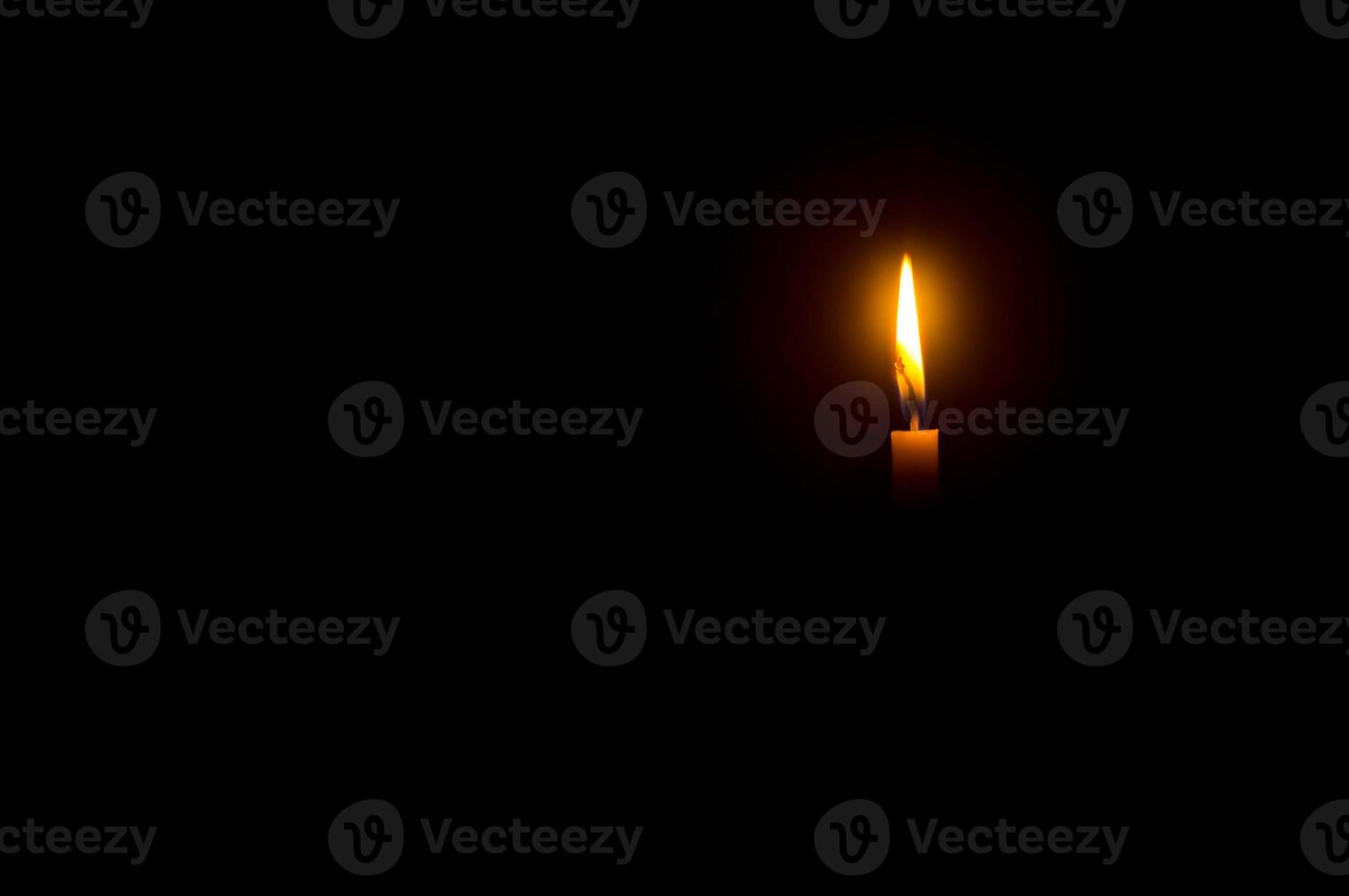 A single burning candle flame or light glowing on an orange candle on black or dark background on table in church for Christmas, funeral or memorial service with copy space photo