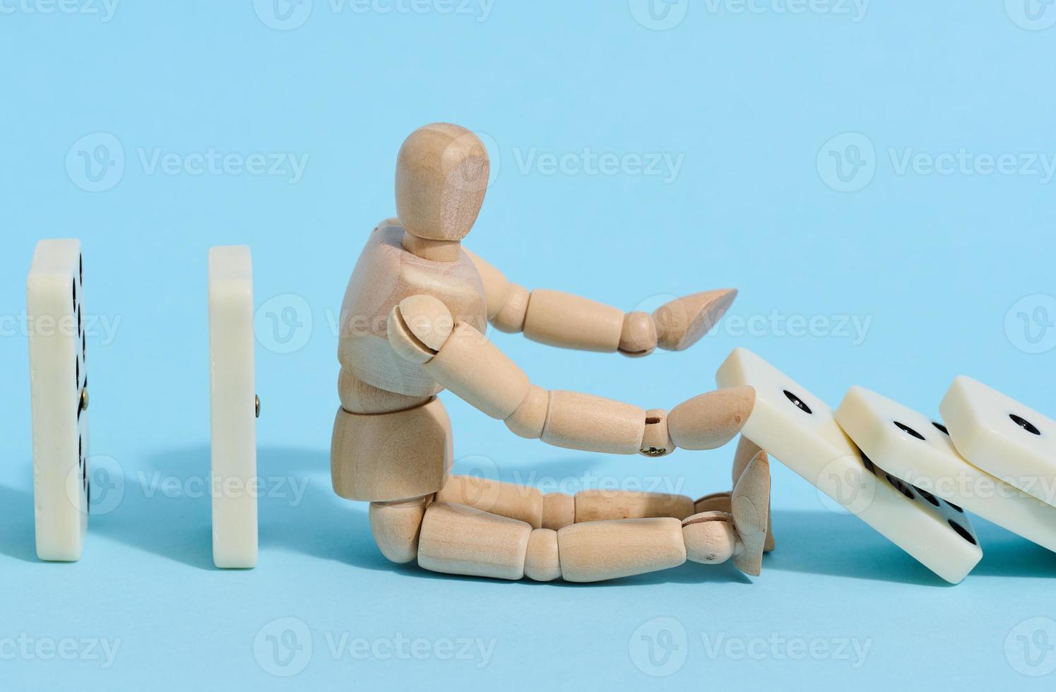 A wooden puppet toy holds back a falling domino on a blue background, representing the concept of a strong personality photo