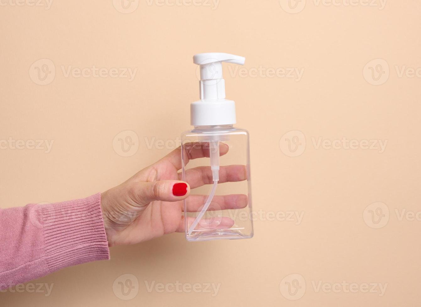 Female hand holds empty plastic container with dispenser for liquid products, soap or shampoo on beige background photo