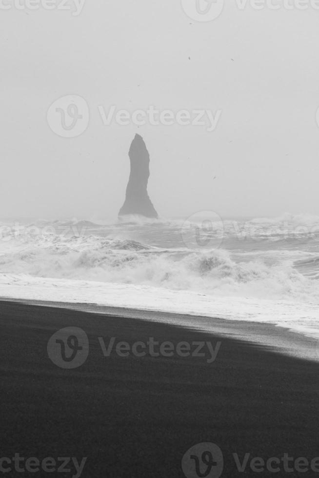 Spiky rock column on beach monochrome landscape photo