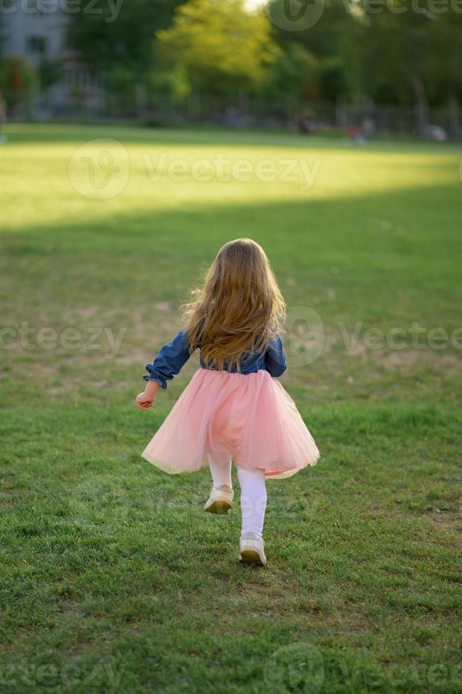 un pequeño niña 3 años antiguo en un verano vestir carreras lejos desde el cámara. el niña es convertido atrás. verano tiempo. foto