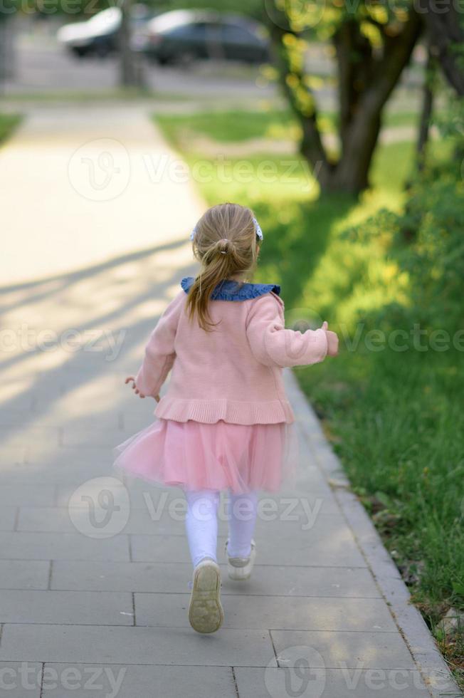 un pequeño niña 3 años antiguo en un verano vestir carreras lejos desde el cámara. el niña es convertido atrás. verano tiempo. foto
