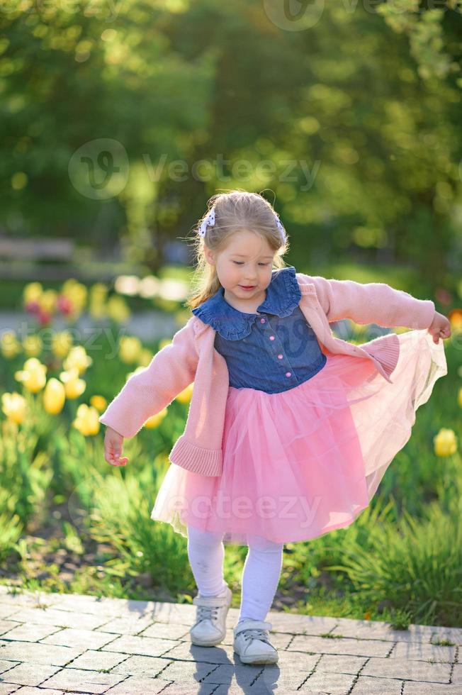 A little girl 3 years old walks in the park in a dress and a pink sweater. photo