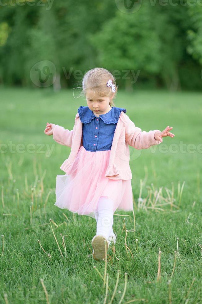 A little girl 3 years old walks in the park in a dress and a pink sweater. photo