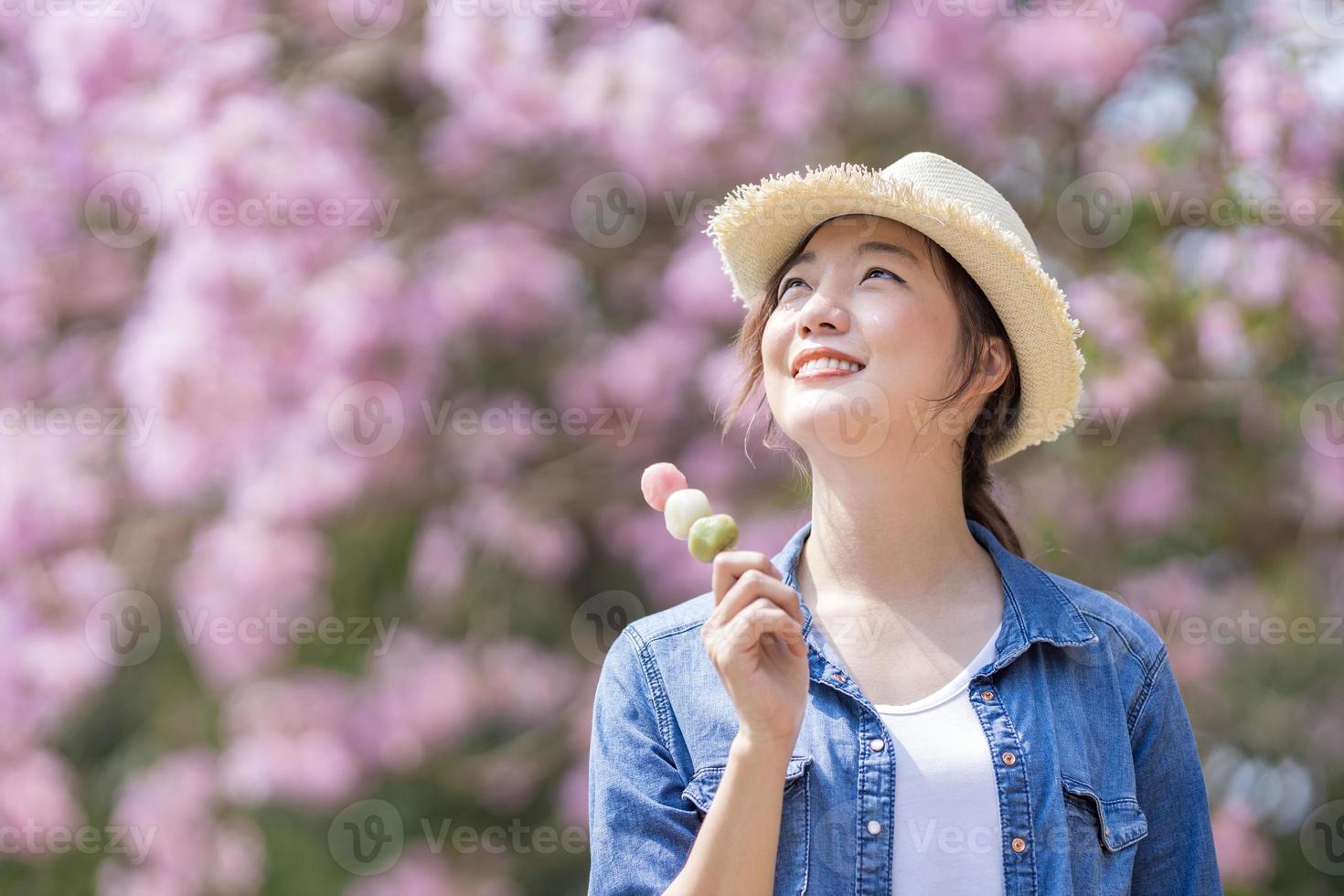 Asian woman holding the sweet hanami dango dessert while walking in the park at cherry blossom tree during spring sakura festival with copy space photo