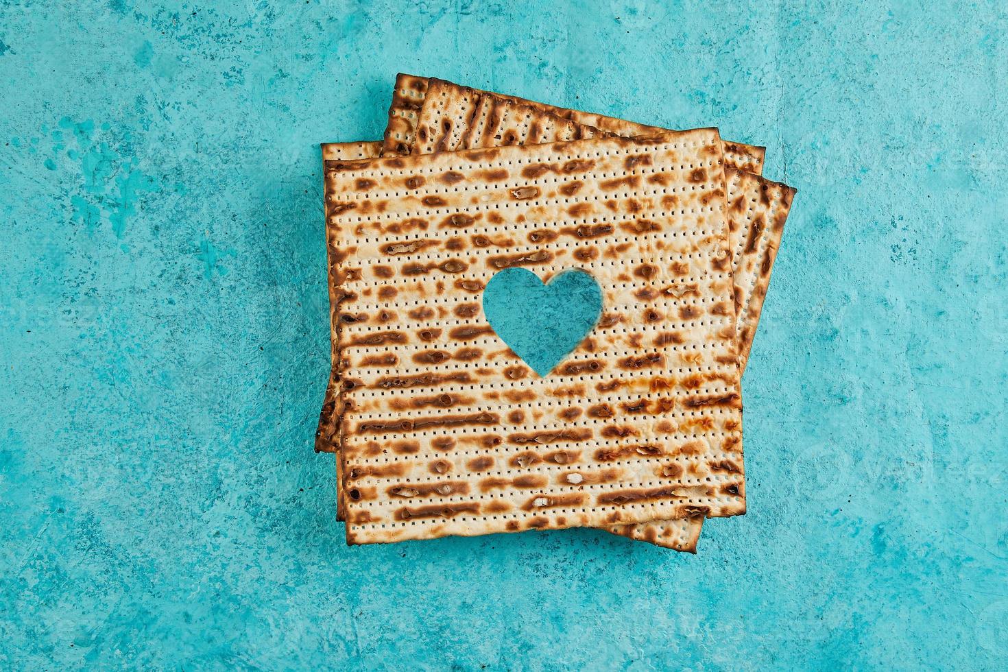 Pesach celebration concept - Jewish holiday Pesach. Matzah squares stacked in a square on blue background. Heart carved in matzah. Flat lay photo