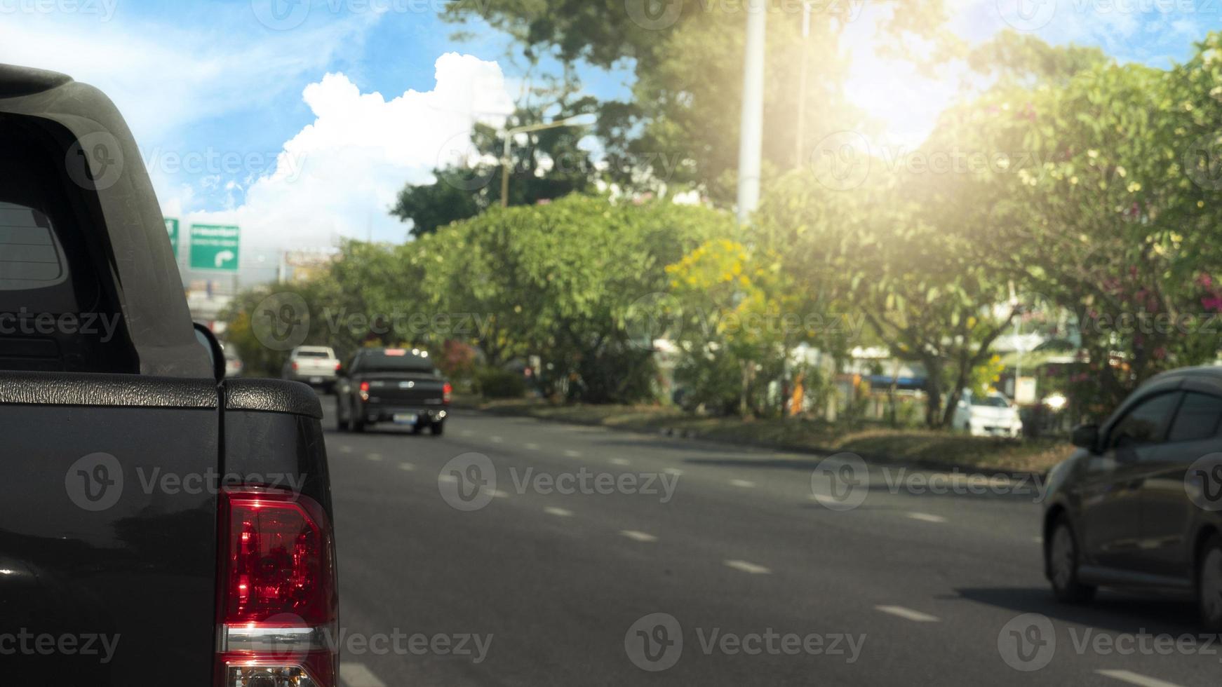 Back side of pick up car bleck color on the asphalt road. Clear streets with few cars. Beside road with trees. and background under of blue sky and white clouds. photo