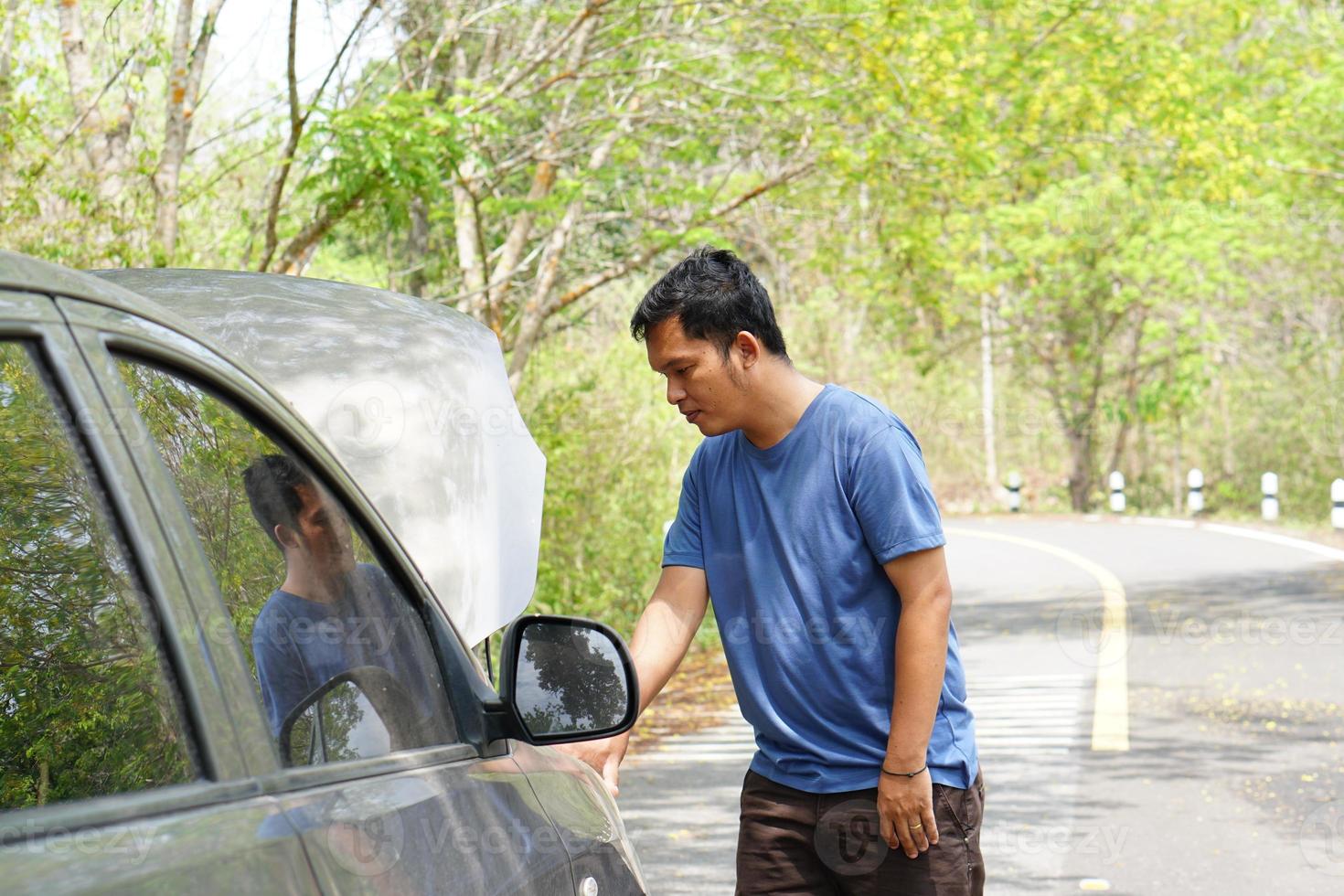 Man looking at a broken car engine on the side of the road photo