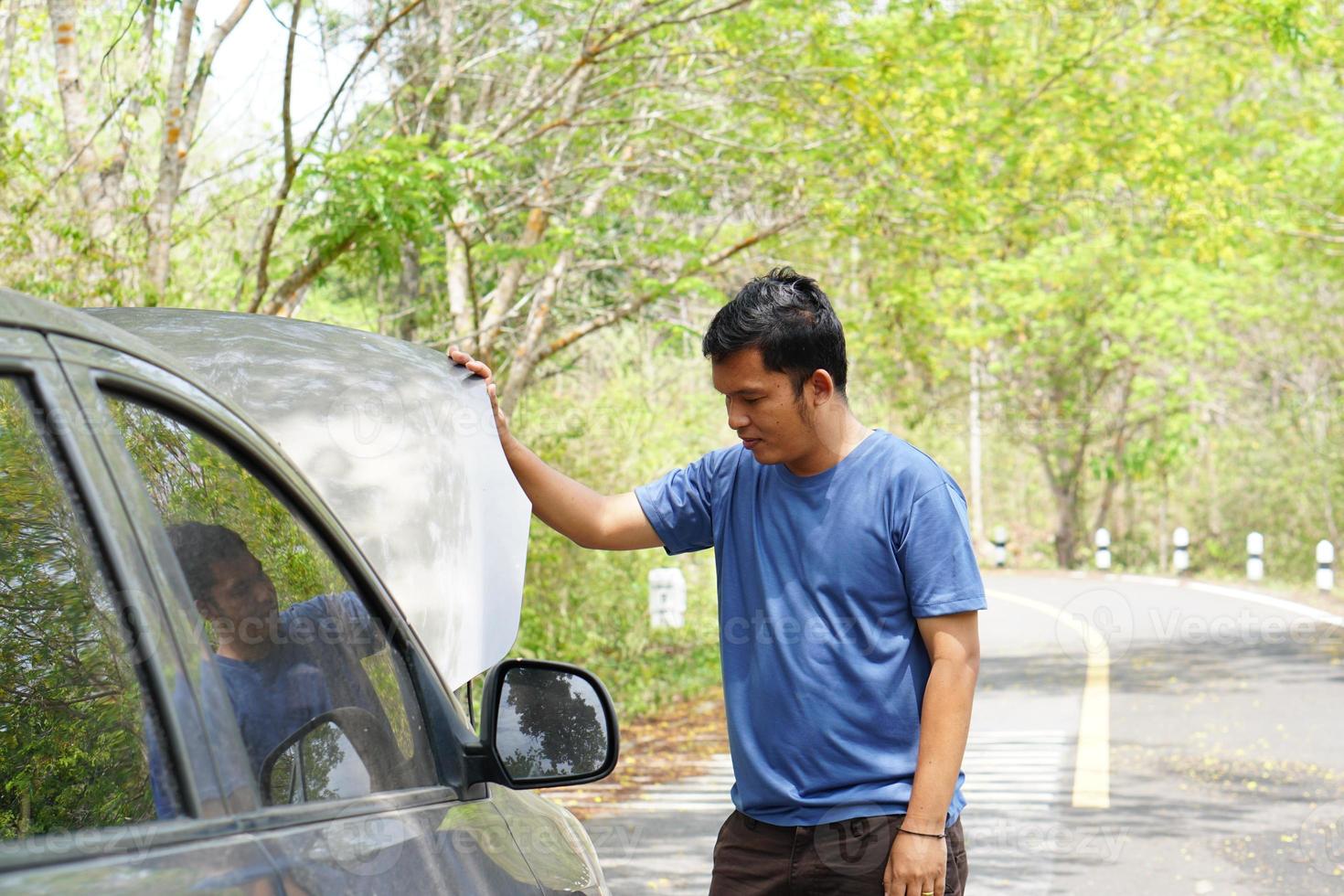 Man looking at a broken car engine on the side of the road photo