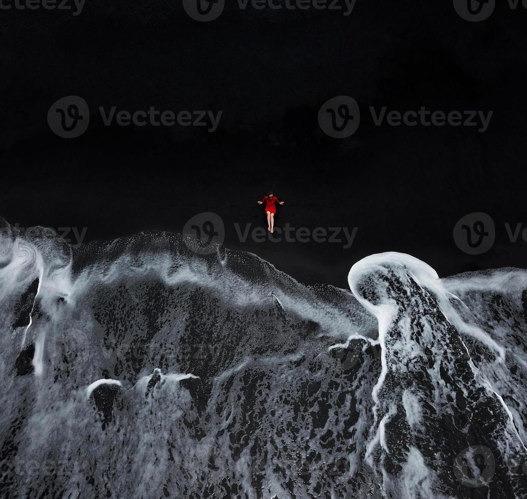 Aerial view of a girl in a red dress sitting on the beach with black sand. Tenerife, Canary Islands, Spain photo