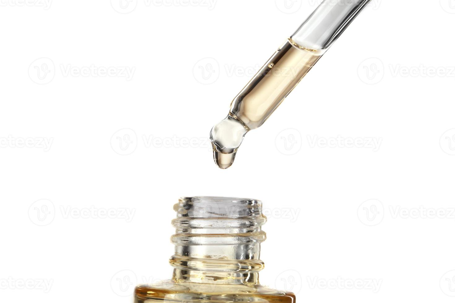 Part of a bottle with yellow cosmetic serum. Cosmetic glass pipette with a yellow oily drop of serum close-up on a white background. photo