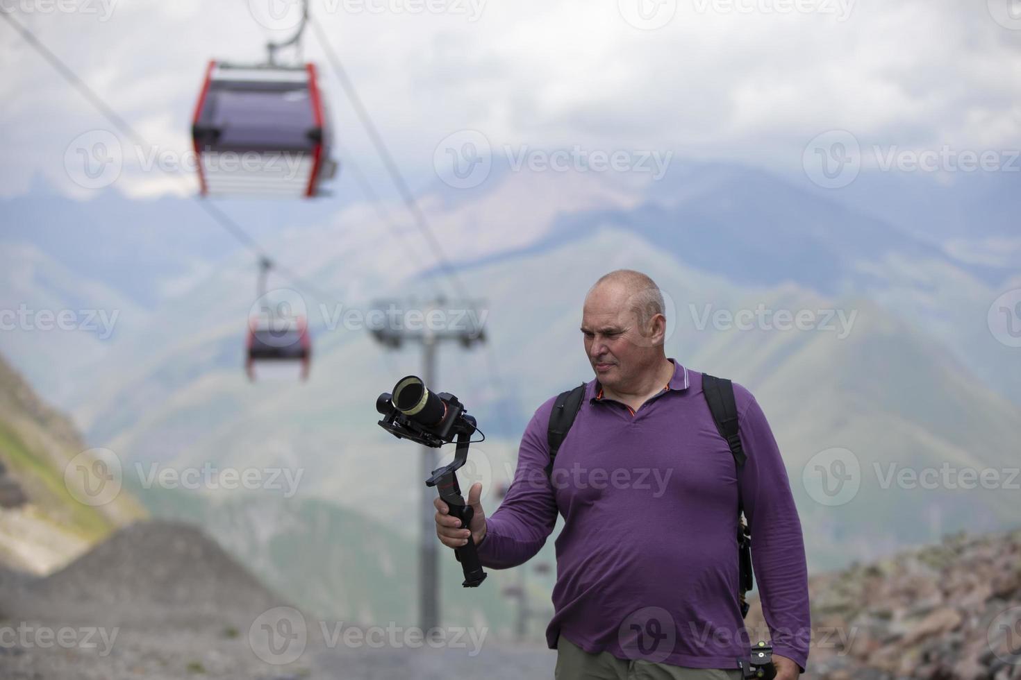 A man is filming a cable car in the mountains with a video camera. A tourist writes a YouTube blog while traveling. photo