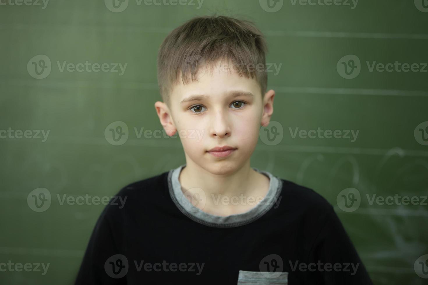 Portrait of a schoolboy at the blackboard. The boy in the classroom is looking at the camera. photo