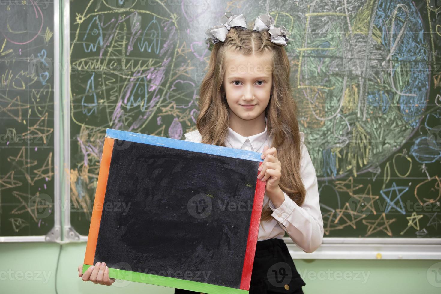 Schoolgirl of middle school age in the classroom holding a drawing board and looking at the camera. photo