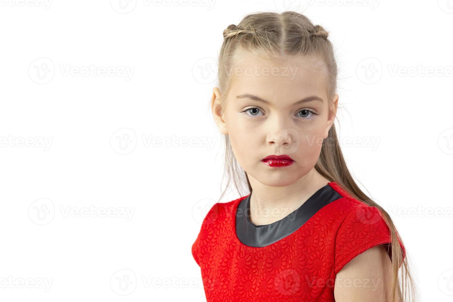 A tenyearold model girl in a red dress with painted lips looks at the