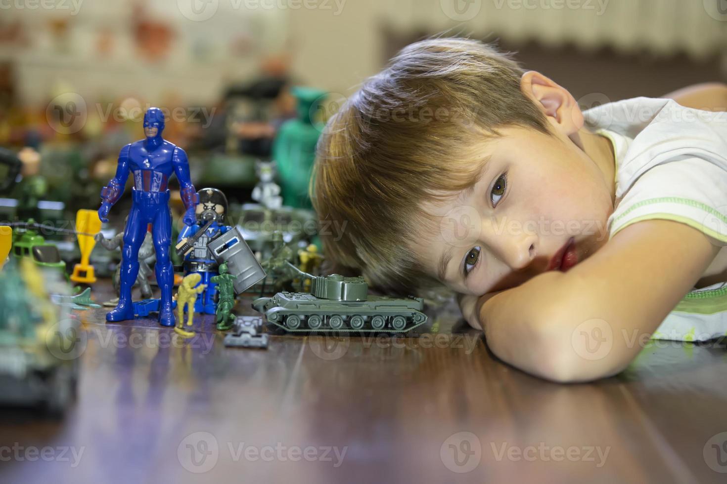 Emotional portrait of an unhappy child lying on a wooden floor with his plastic block toy, Shot of a bored child's face. photo