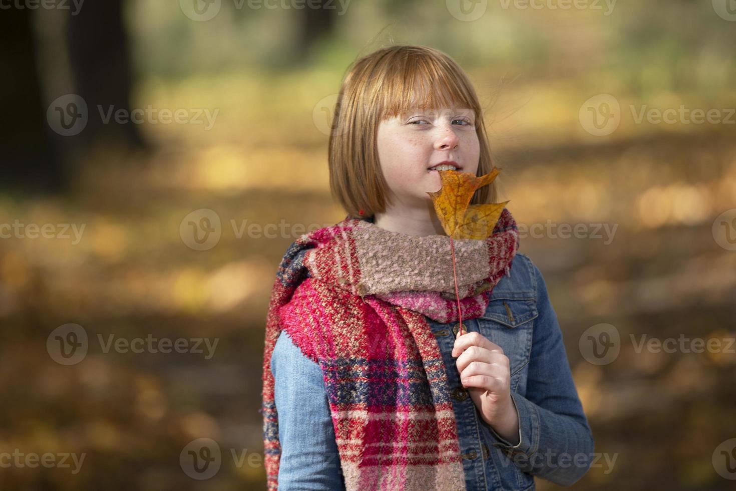 Happy red-haired girl with maple leaf in autumn park. photo