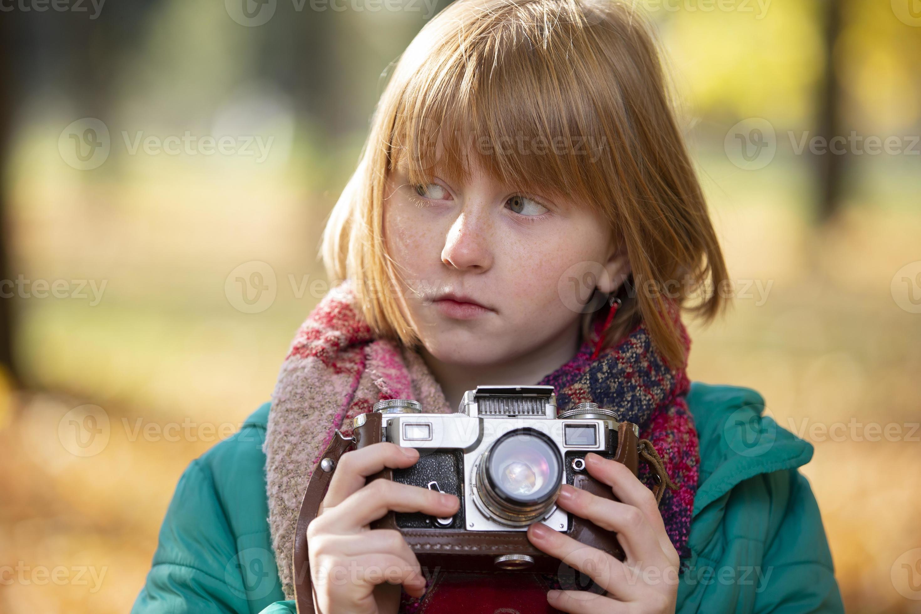 Little redhaired girl with a retro camera in the autumn park. Child