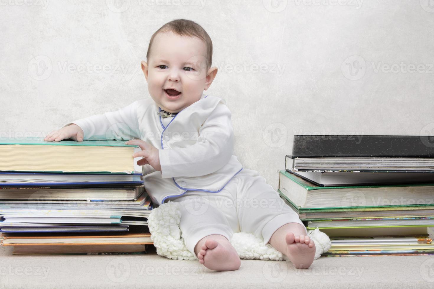 Little child among books. Happy six month old baby boy in a stack of books. The concept of early childhood education. photo