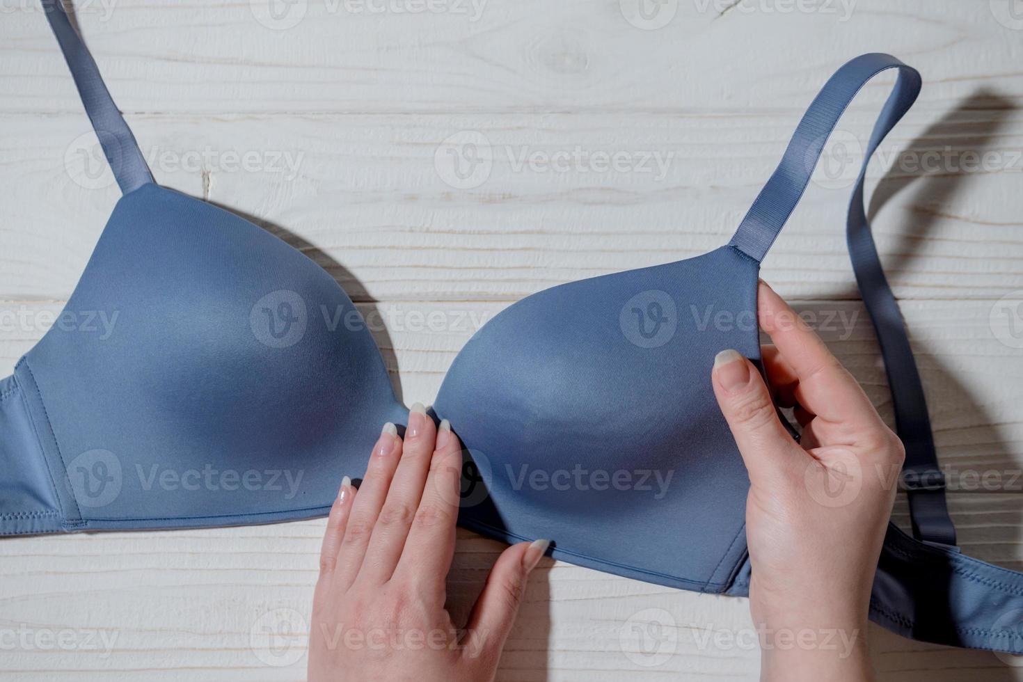 Woman holding blue bra, wooden background, closeup photo
