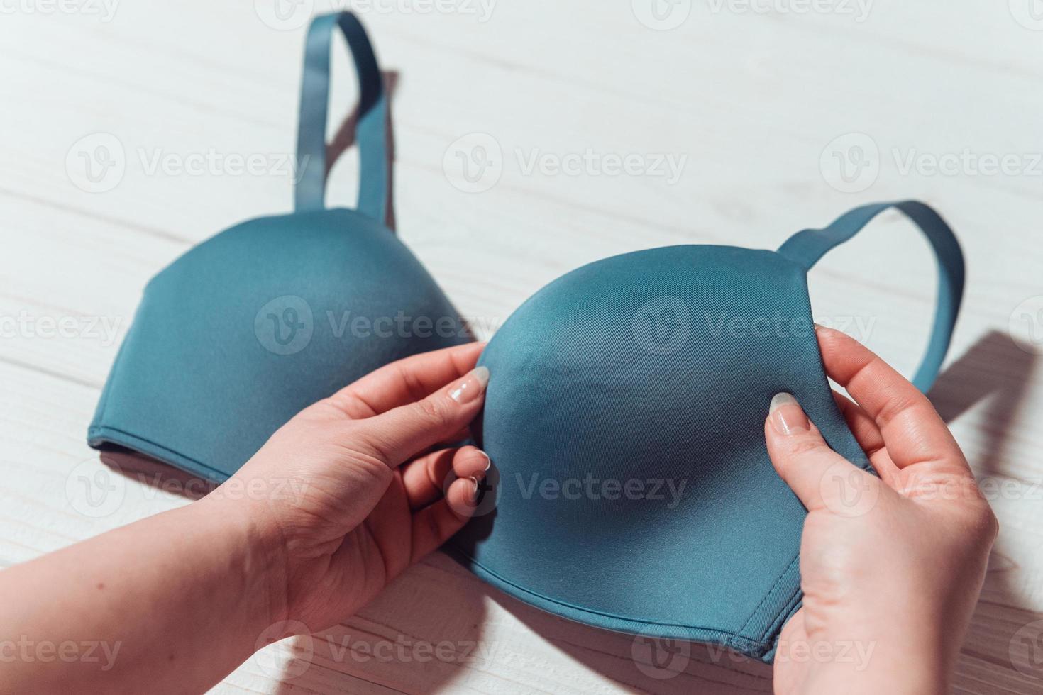 Woman holding blue bra, wooden background, closeup photo