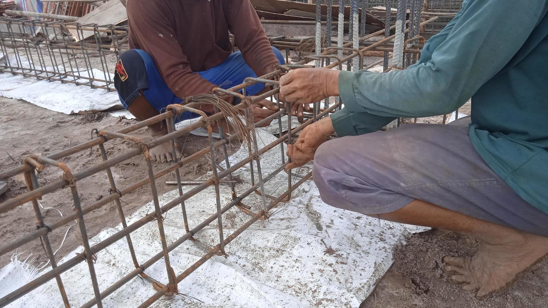 Worker's hands stringing iron rods with wire for beam section photo