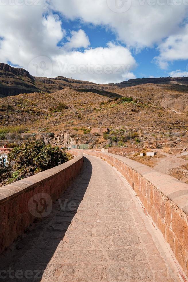 Footpath on dam leading towards rocky mountain landscape photo