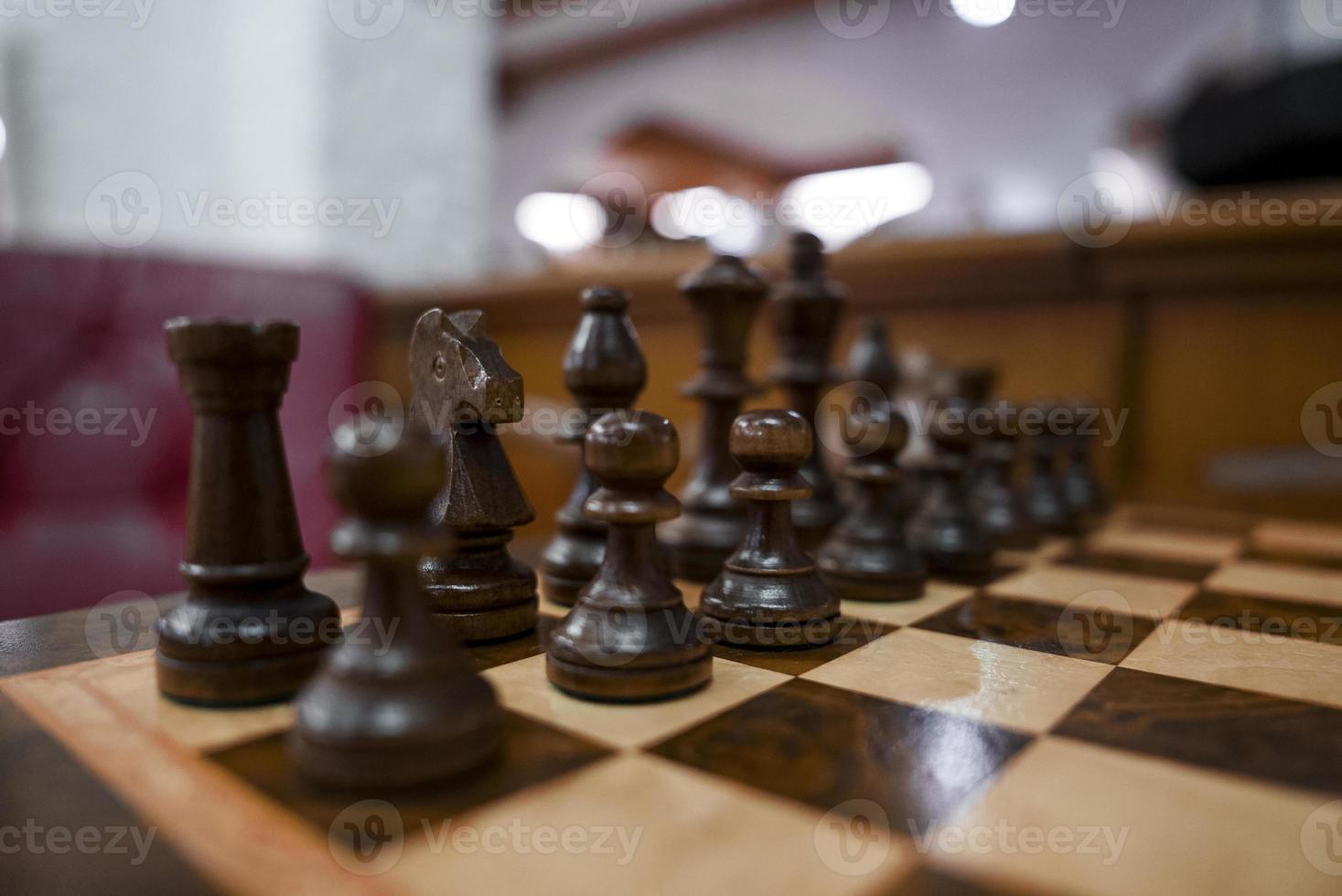 Closeup of brown wooden chess pieces arranged on chessboard in hotel photo