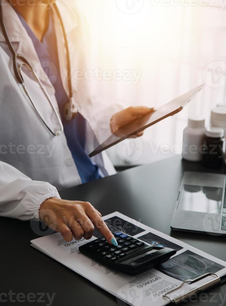 Doctor working with laptop computer and writing on paperwork. Hospital background. photo