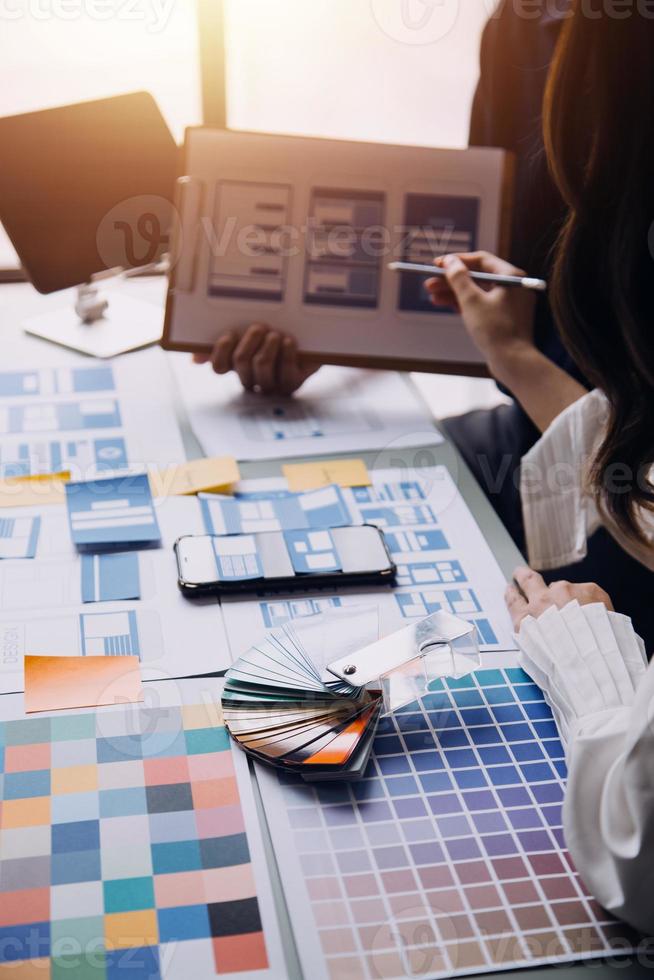 Close up ux developer and ui designer brainstorming about mobile app interface wireframe design on table with customer breif and color code at modern office.Creative digital development agency photo