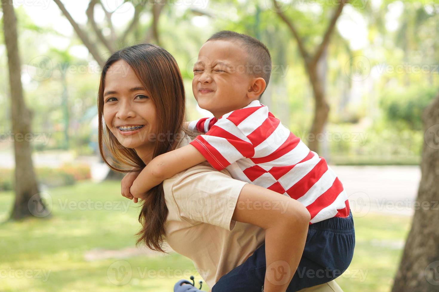 A boy happily rides on his mother's back in the park. photo