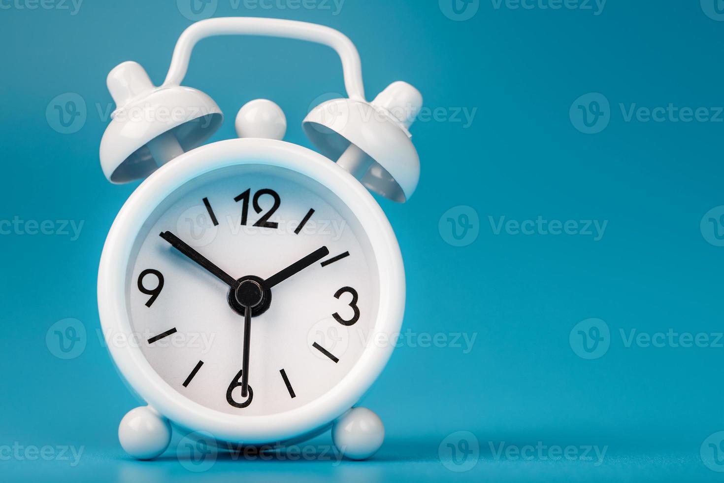 White retro alarm clock on blue background. Concept of time with free space for text. photo