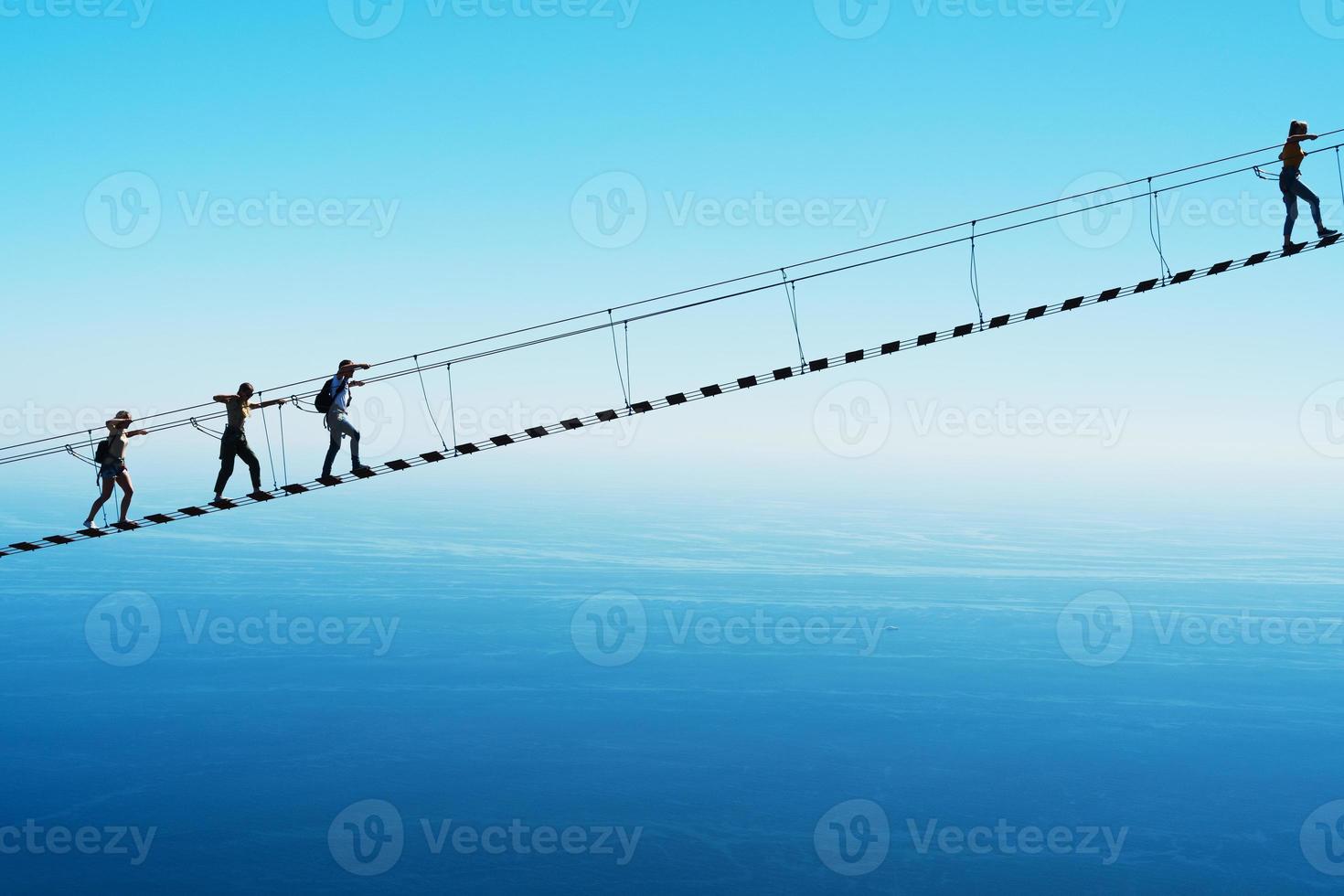 A suspension bridge over a cliff on the background of the sky with people climbing up. Selective focus photo