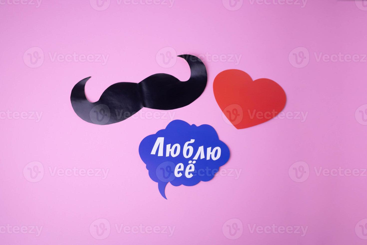 On a pink paper background, a black mustache, a red heart, a blue cloud with the words I love her photo