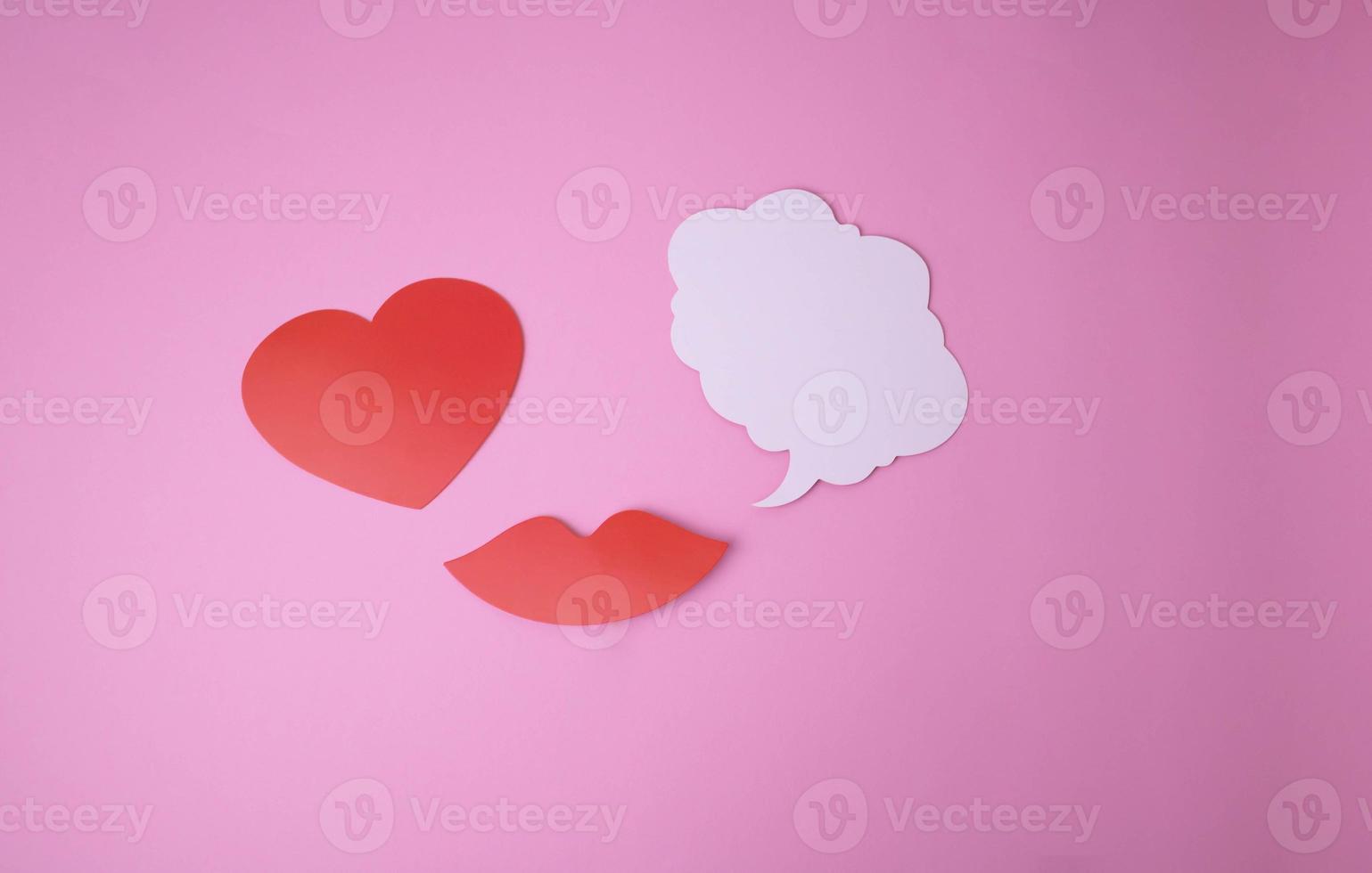 On a pink background paper red lips and a heart and a white cloud for words. photo