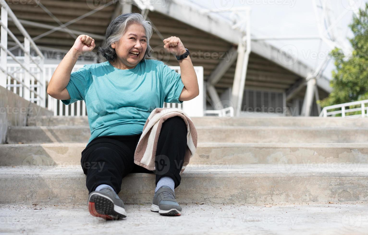 feliz y sonriente anciana asiática sentada en las escaleras para descansar después del entrenamiento, trotar por la mañana, hacer ejercicio al aire libre para una buena salud. concepto de salud y estilo de vida activo para una vida saludable foto