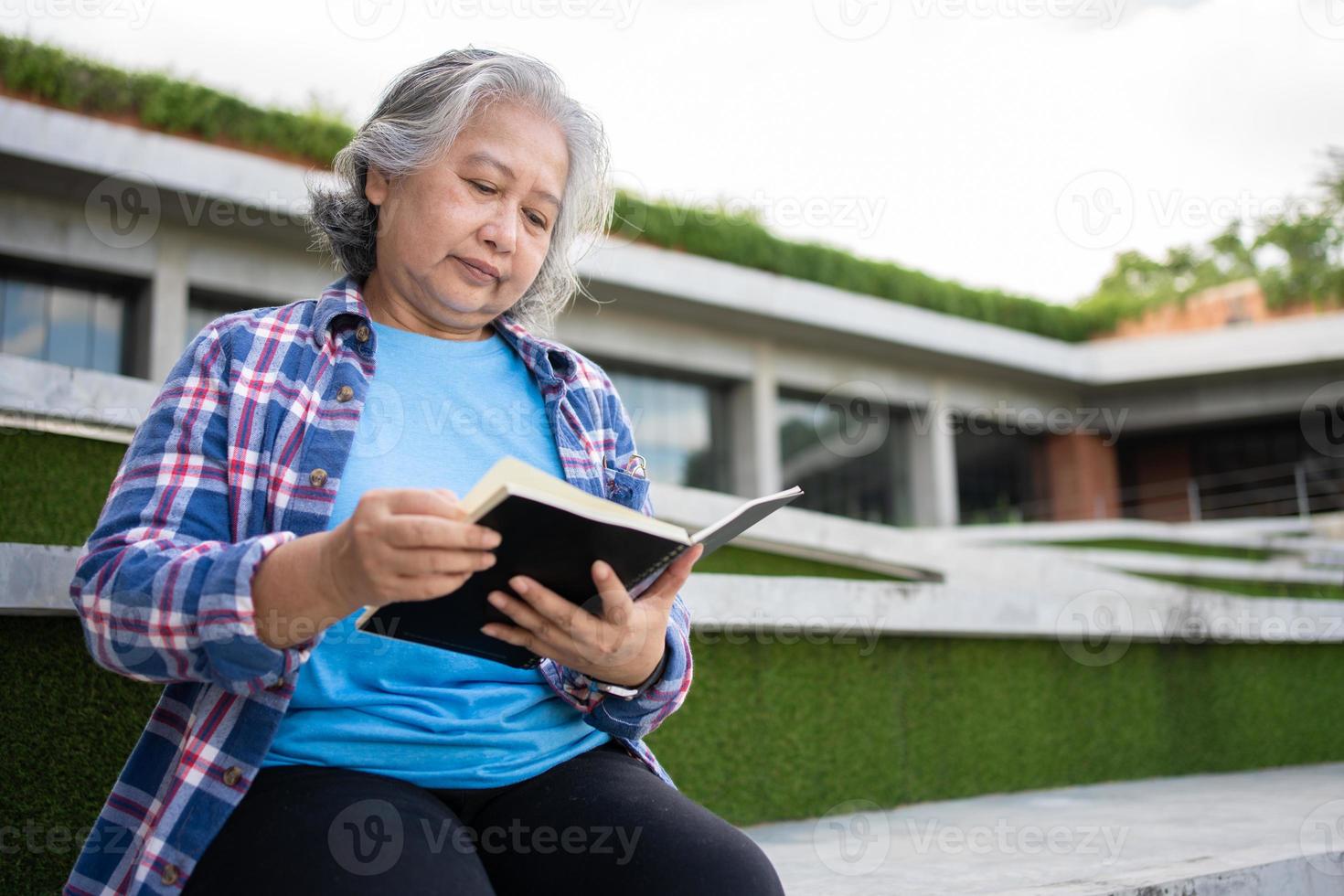 maduro adulto estudiante sentado en frente apagado Universidad edificio y leyendo colegio libros después asistiendo un Universidad clase, adulto educación aprendizaje estudiando contento asiático mayor retirado actividad foto
