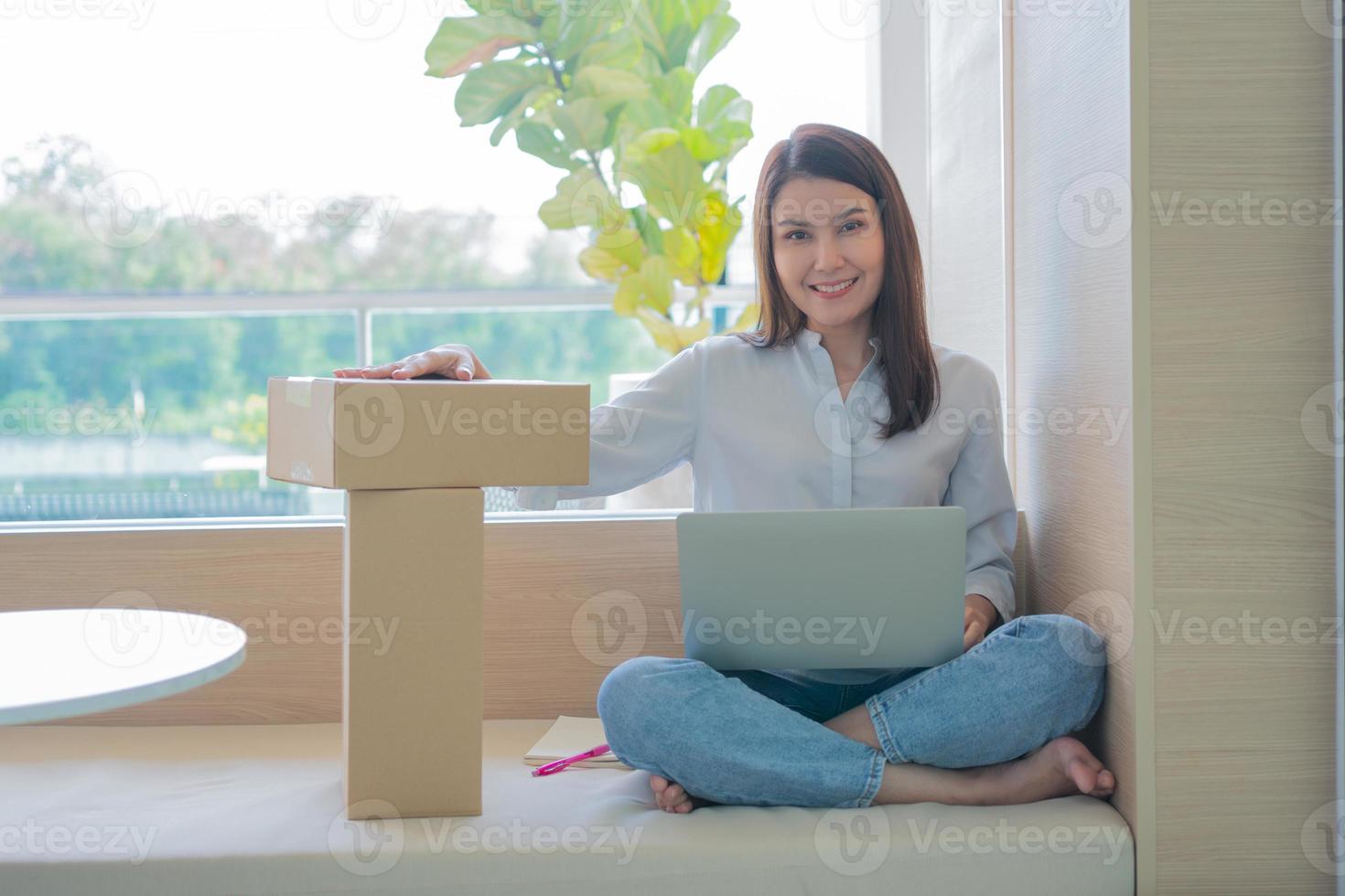 Happy young Asian woman entrepreneur, Hold package and Smile for sale success of online shopping store at home office, Concept of merchant, small business, online business and eCommerce. photo