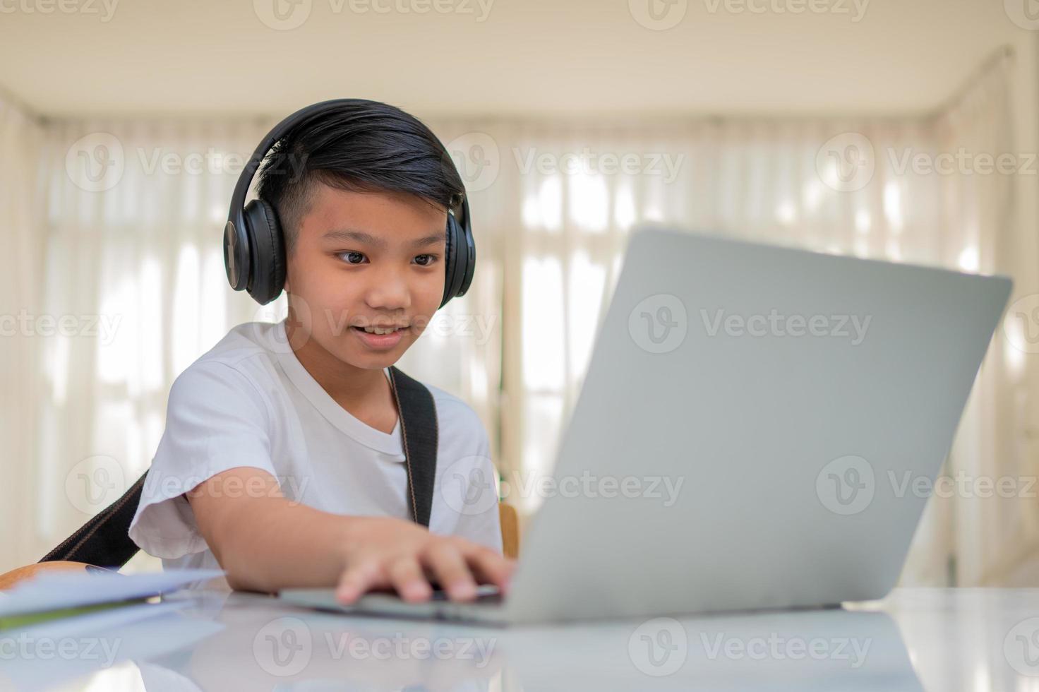 Asian boy playing guitar and watching online course on laptop while practicing for learning music or musical instrument online at home. Boy students study online with video call teachers play guitar. photo