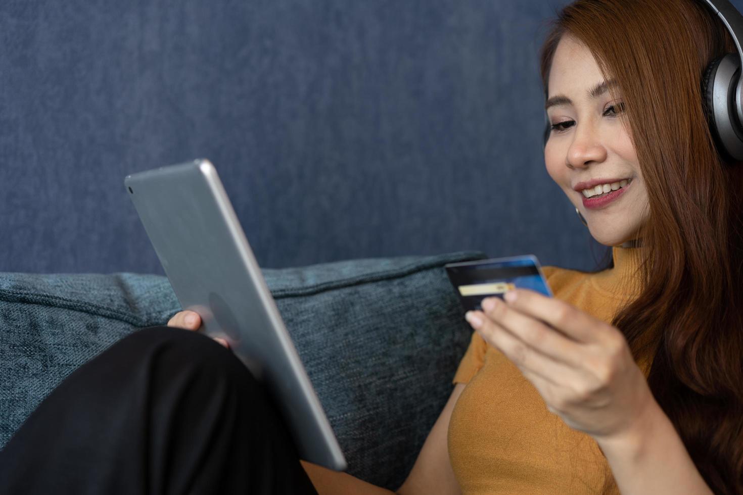 Portrait of young woman wear headphones and holding tablet and banking credit card, transferring money online, shopping goods in internet store, purchasing services, satisfied with secure payments. photo