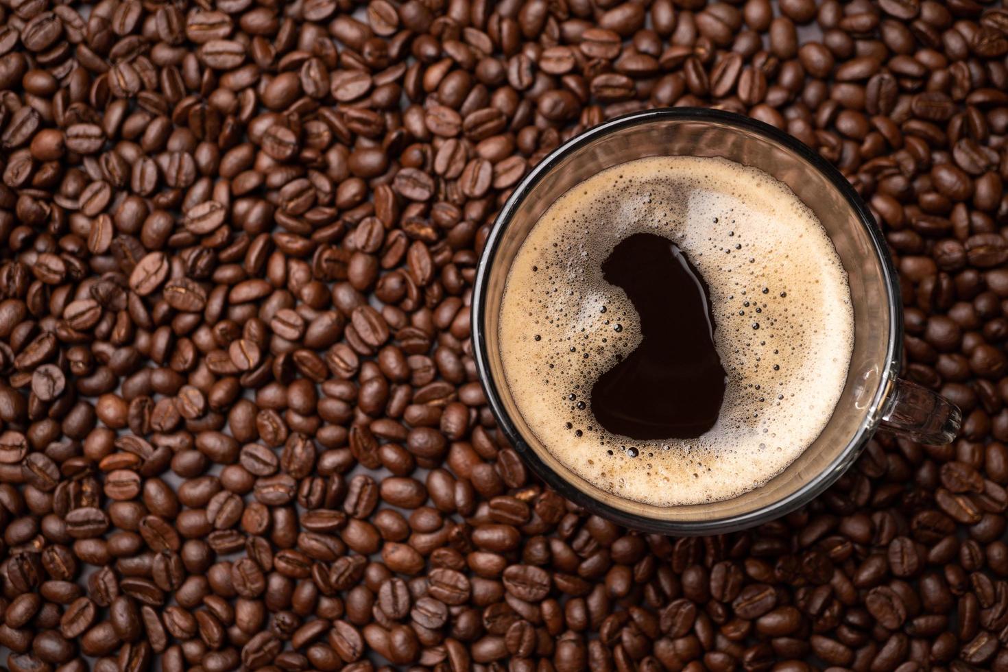 The top view of a coffee cup and group of black coffee beans is the background. Strong black espresso, Grounds of coffee background, texture photo