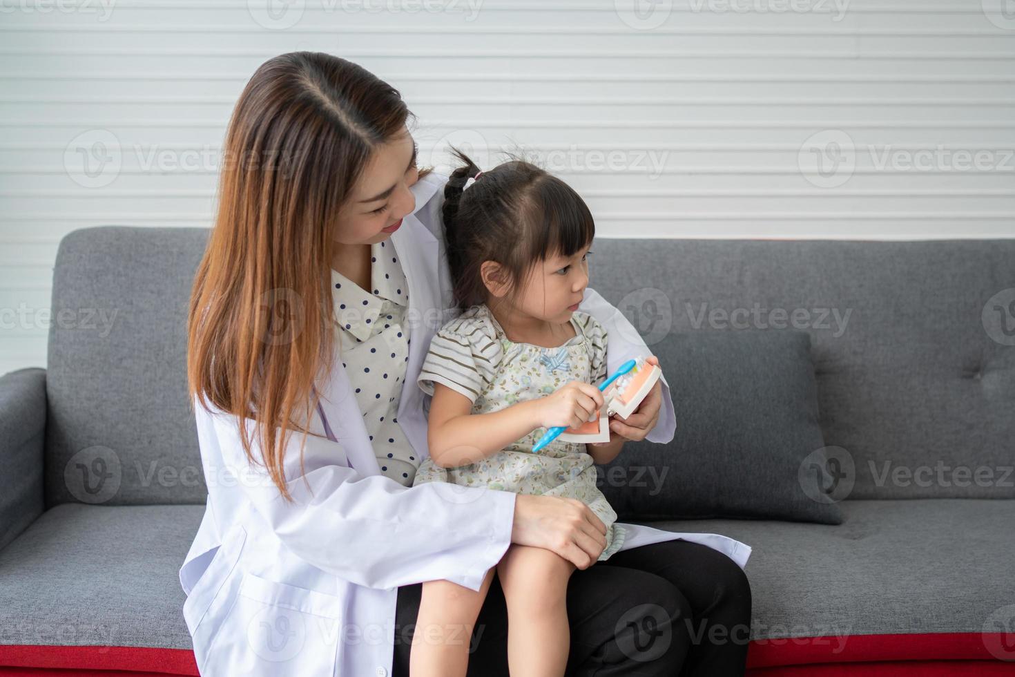 Asian female dentist teaching cute little girl brushing teeth with toothbrush and stomatologist telling girl child about oral hygiene in dental clinic, Education and prevention cavities concept. photo