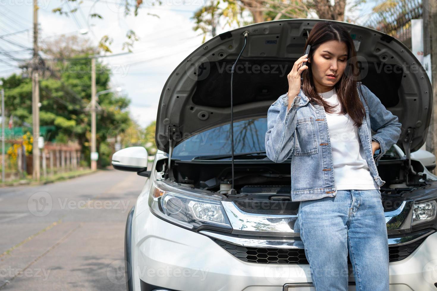 mujer asiática enojada y usando un teléfono móvil pidiendo ayuda después de una avería en el coche en la calle. concepto de problema del motor del vehículo o accidente y ayuda de emergencia de un mecánico profesional foto