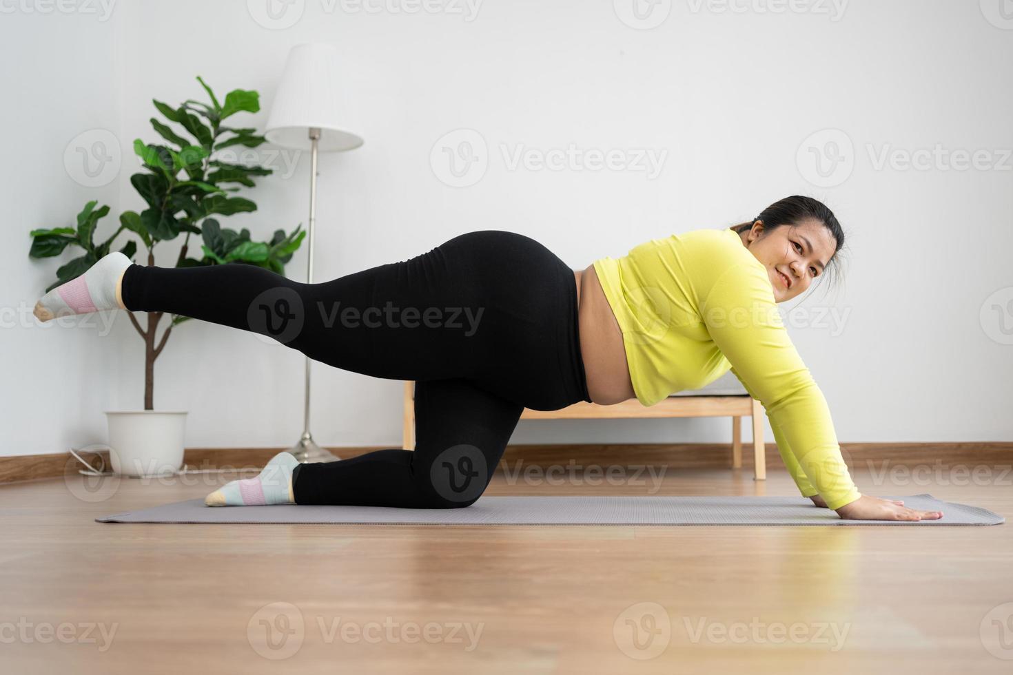 Asian overweight woman doing stretching exercise at home on fitness mat. Home activity training, online fitness class. Stretching training workout on yoga mat at home for good health and body shape. photo