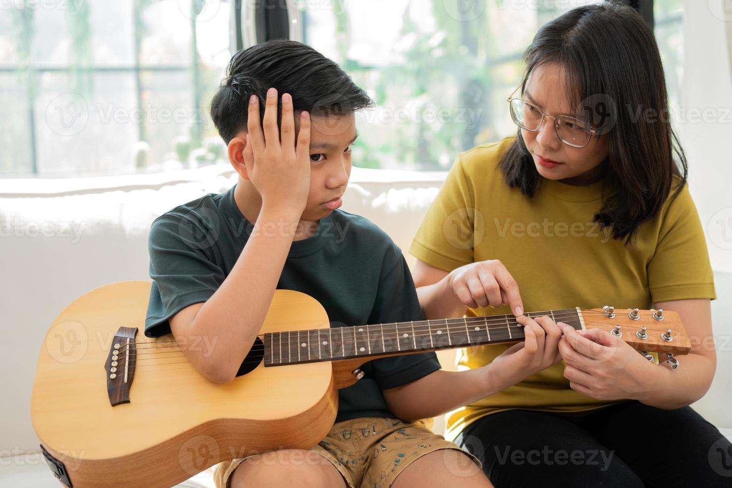 Asian mother embraces son, Asian boy playing guitar and mother embrace on the sofa and feel appreciated and encouraged. Concept of a happy family, learning and fun lifestyle, love family ties photo