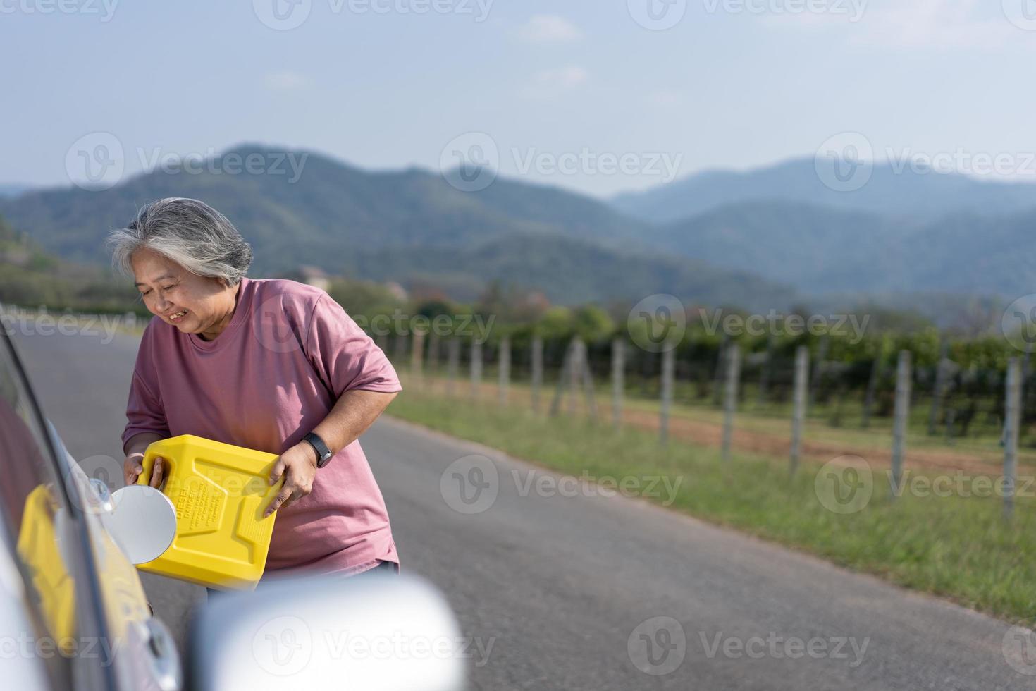 The car ran out of gas and stalled beside the road in suburbs and an elderly Asian woman used a gallon of spare gas to fuel the car. A woman prepares a gallon of spare gas to fuel before traveling. photo