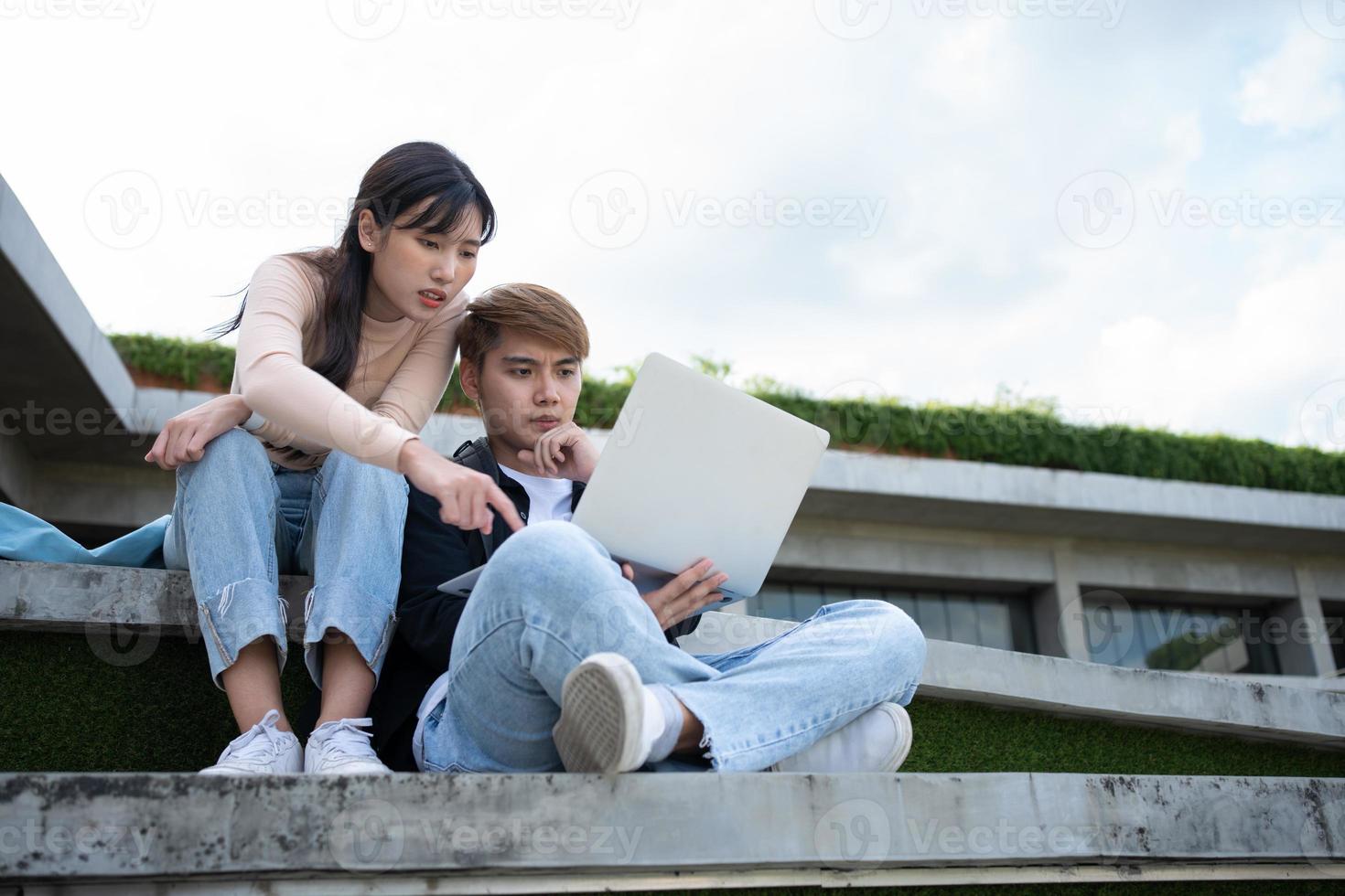 Asian students sitting on steps and use computer laptops to discuss before exams, Student lifestyle at university. Group of student do a project together photo
